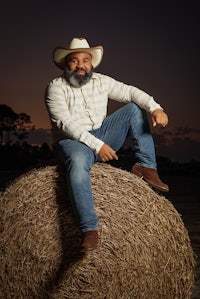 a man in a cowboy hat sitting on top of a hay bale