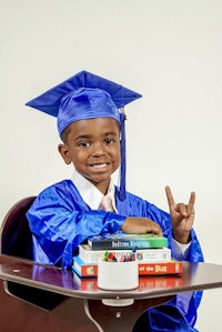 a young boy in a graduation cap and gown sitting at a desk